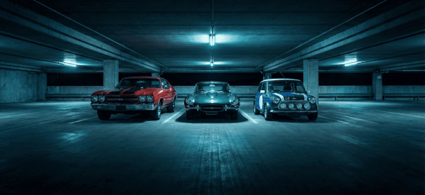 Trois voitures de collection (Chevrolet Chevelle, Jaguar Type E, Mini Cooper) stationnées dans un parking souterrain - cibles fréquentes de vol