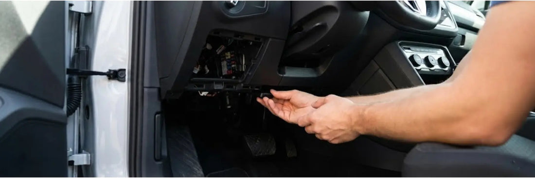 Main plaçant un traceur GPS miniature sous le tableau de bord d'une voiture